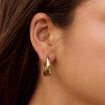 Valentina Gold Hoop Earrings, worn on an ear with long dark hair, polished gold hoop
