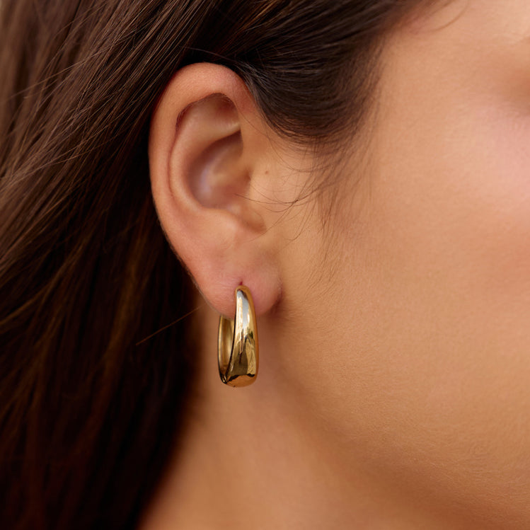 Valentina Gold Hoop Earrings, worn on an ear with long dark hair, polished gold hoop